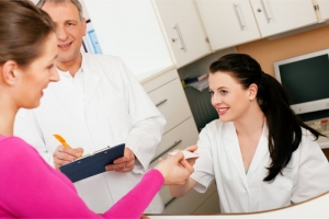 lady handling her health insurance card to a nurse while the doctor is writing on a clipboard